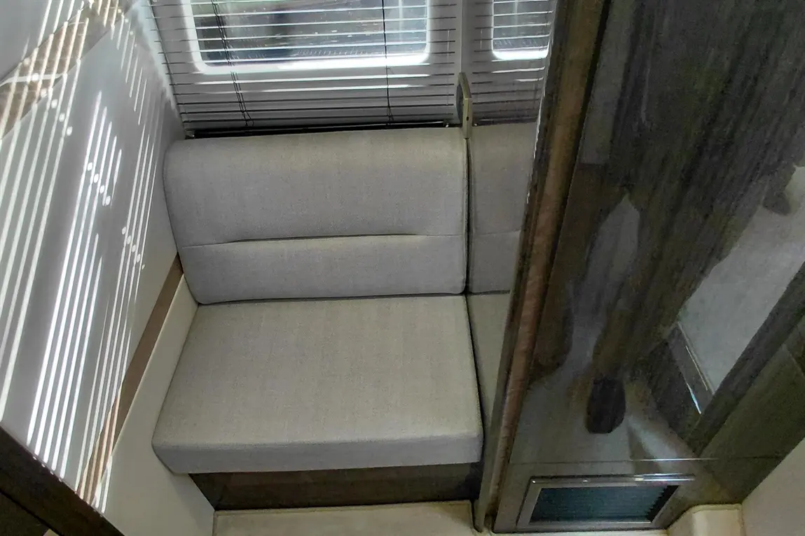 A grey upholstered seat nestled in a small, well-lit area, with sunlight casting patterns through blinds.